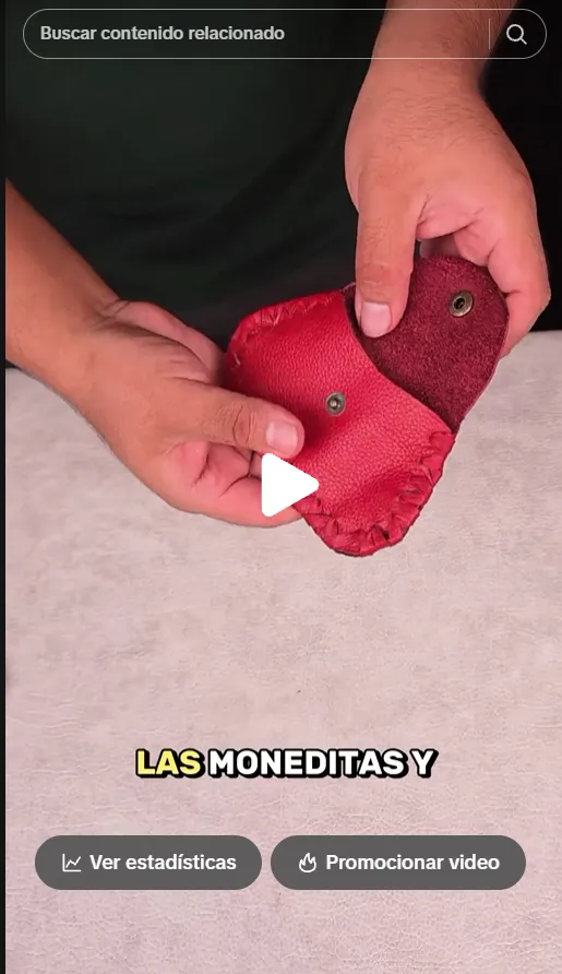Manos del artesano mostrando un monedero rojo de cuero con broche y costura en el borde.
